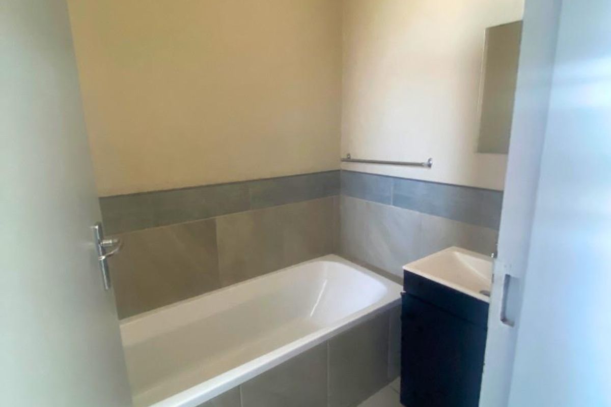 A functional bathroom featuring a built-in bathtub with tiled surround, a modern vanity unit, and neutral wall finishes.