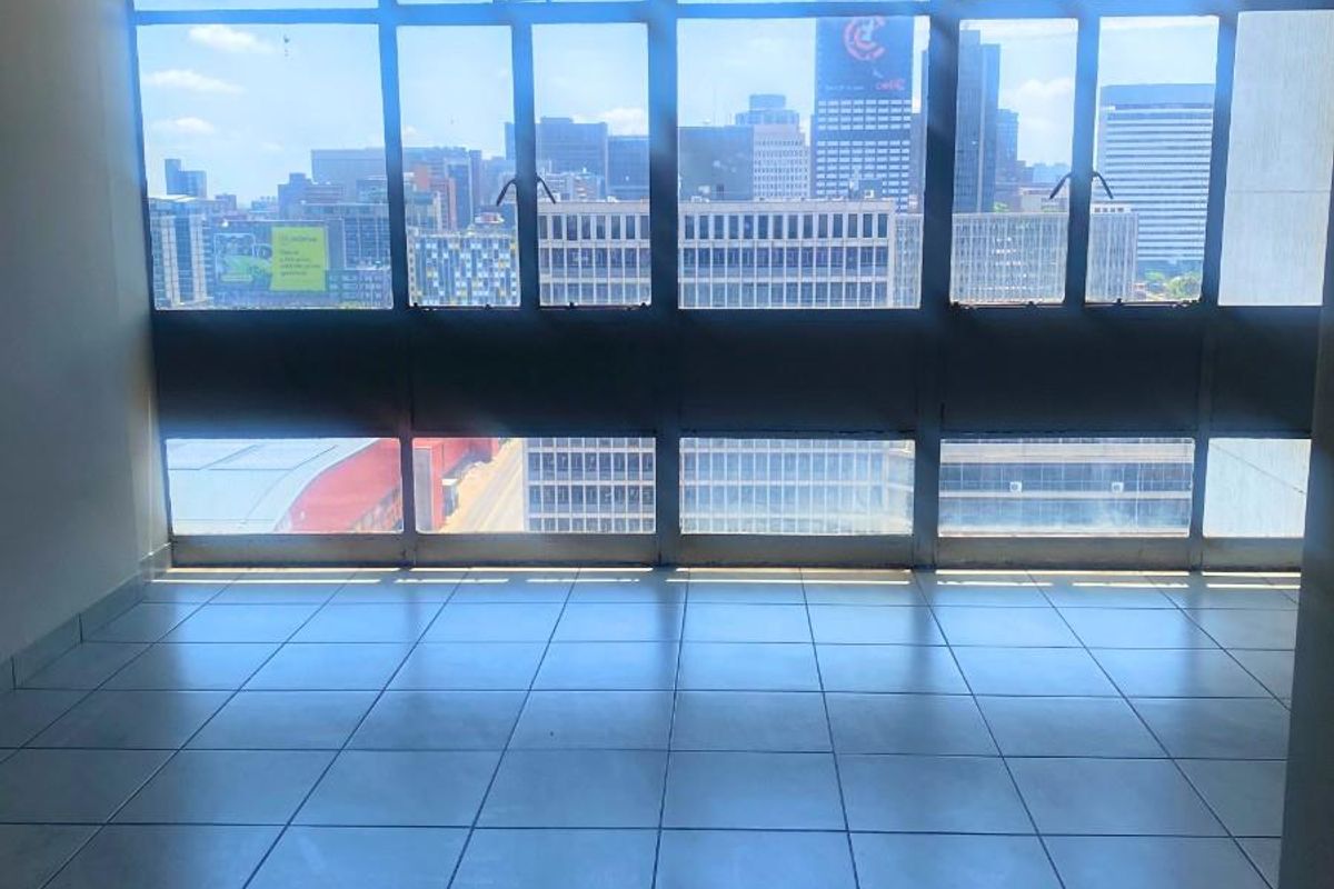 An empty living area featuring large floor-to-ceiling windows that provide an expansive urban city view.