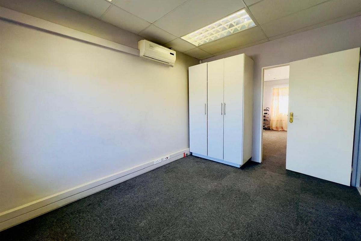 A functional bedroom featuring a built-in wardrobe, wall-mounted air conditioning unit, and carpeted flooring, with direct access to an adjacent room.