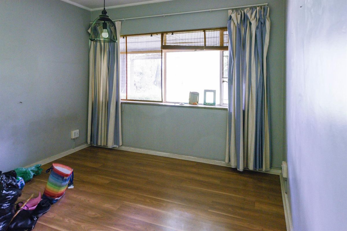 An empty bedroom featuring laminate flooring, neutral wall paint, and a window with fitted curtain tracks.