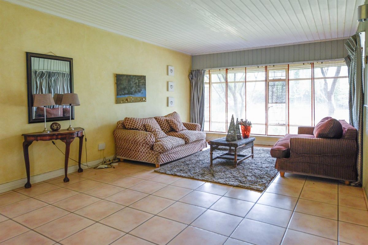 A spacious living room featuring tiled flooring, a timber panelled ceiling, and a large window allowing for natural light.