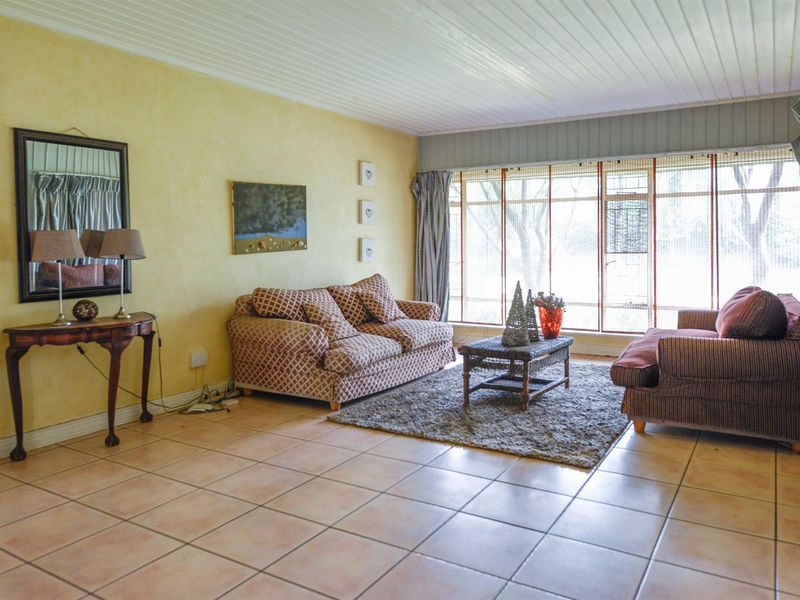 A spacious living room featuring tiled flooring, a timber panelled ceiling, and a large window allowing for natural light.