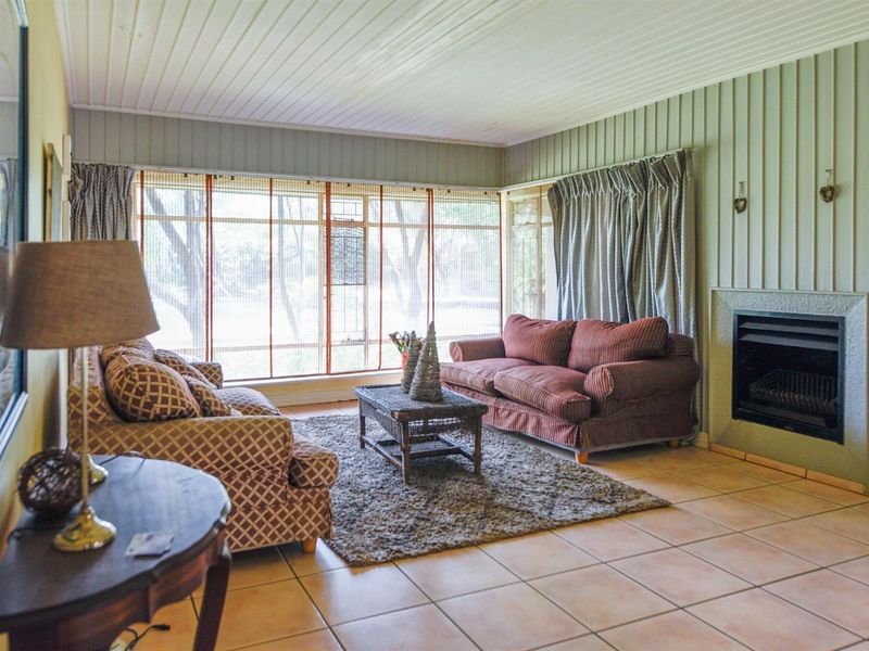 A spacious living room featuring tiled flooring, timber wall paneling, and a built-in fireplace, with large windows providing ample natural light.