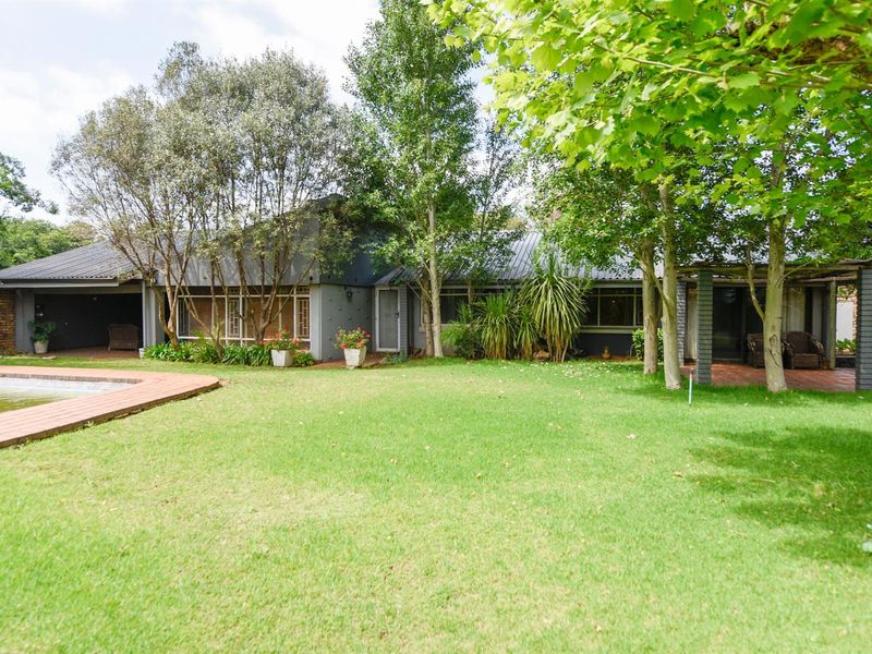 Rear view of the house featuring a spacious lawn, swimming pool, and a covered patio area with mature trees.