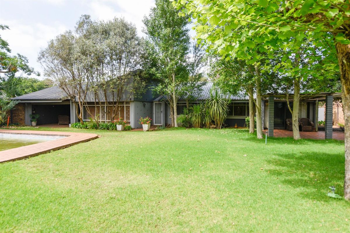 Rear view of the house featuring a spacious lawn, swimming pool, and a covered patio area with mature trees.