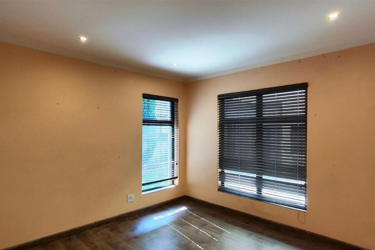 A bright, empty bedroom featuring dark wood-look flooring, recessed ceiling lighting, and dark horizontal window blinds.