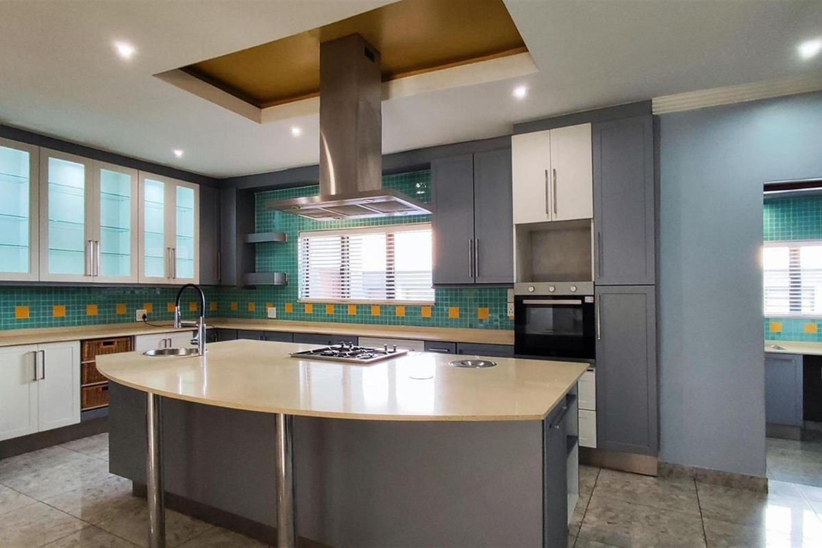 Modern kitchen featuring a large central island with a built-in gas hob, stainless steel extractor fan, tiled backsplash, and ample cabinetry.