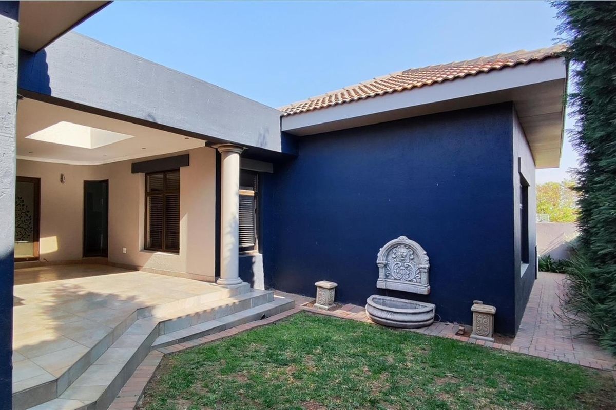 A well-maintained rear patio area featuring a covered terrace, tiled flooring, a decorative wall fountain, and a small landscaped garden.