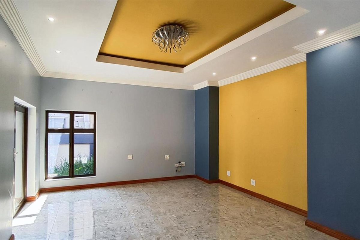 A spacious living room featuring tiled flooring, a decorative recessed ceiling with integrated lighting, and a modern color-blocked wall design.