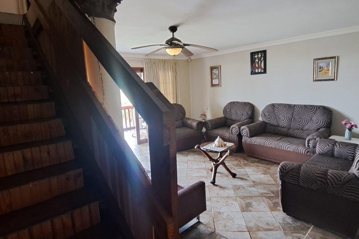 Spacious living area featuring tiled flooring, a central ceiling fan, and a prominent wooden staircase leading to the upper level.