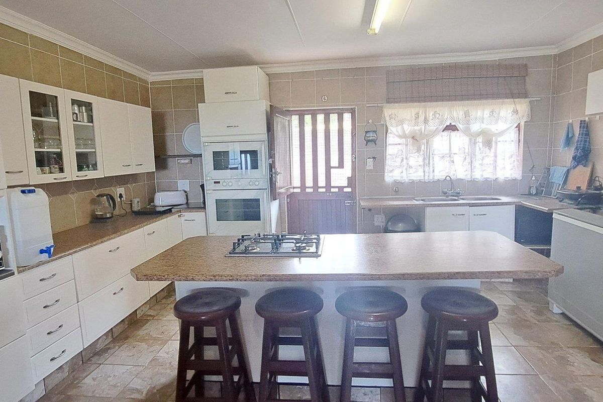 Spacious kitchen featuring a central island with a built-in gas hob, ample cabinetry, and tiled flooring throughout.
