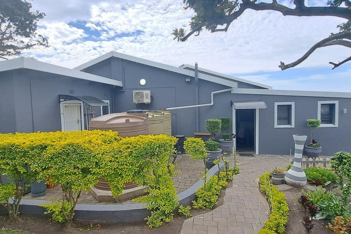 Rear exterior view of the property featuring a paved courtyard, landscaped garden beds, and installed water storage tanks against the main building structure.