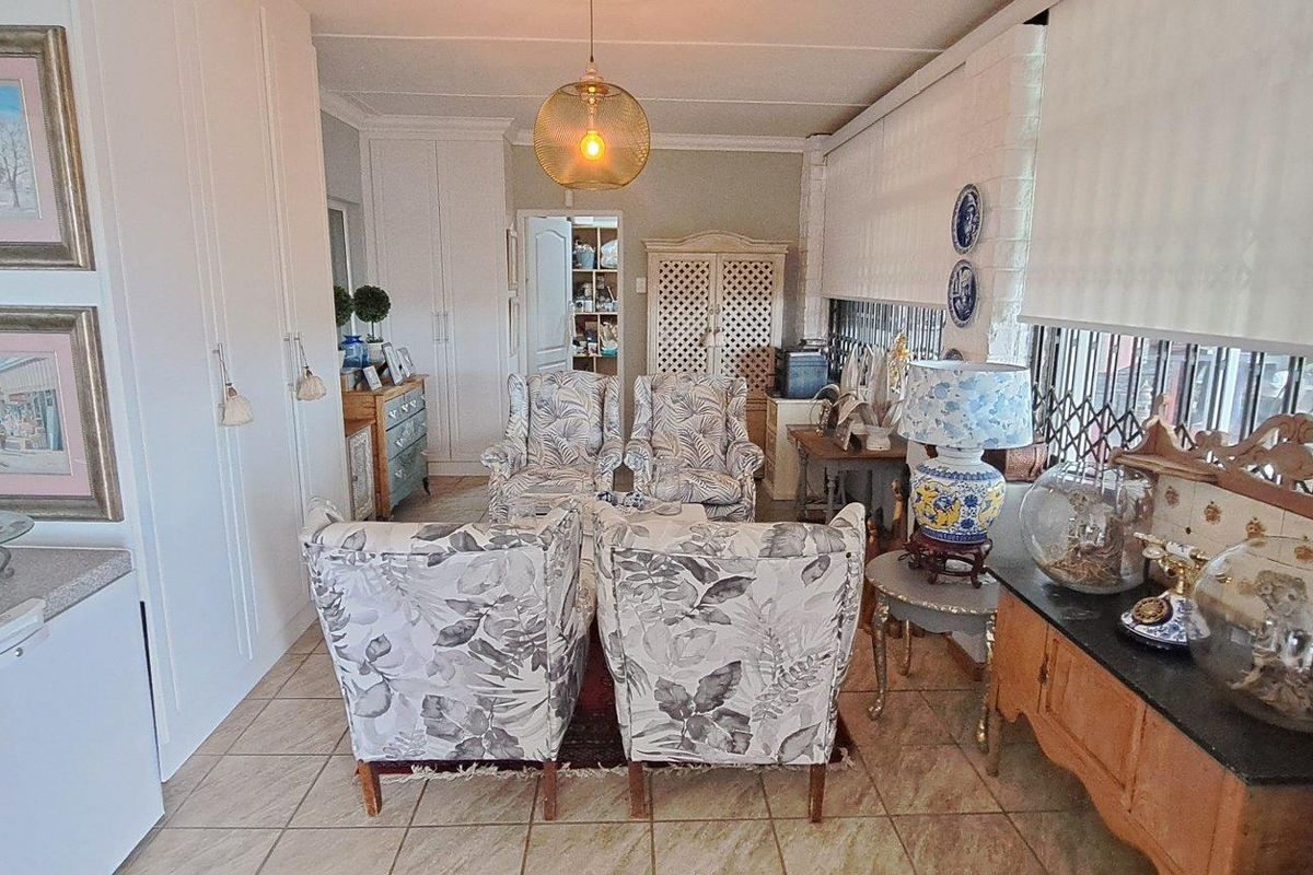 A living area featuring tiled flooring, built-in storage cupboards, and large windows with roller blinds and security gates.