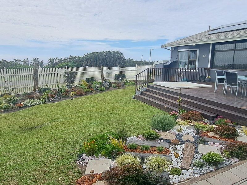 A well-maintained rear garden featuring a timber deck, landscaped flower beds, and a white picket fence with a view of the surrounding area.