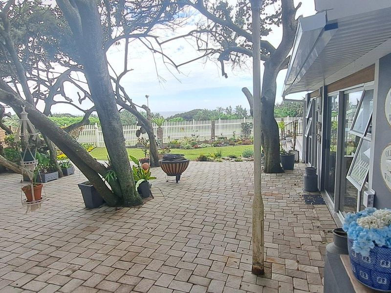 A paved outdoor patio area featuring mature trees, sliding glass door access to the home, and a white picket fence boundary.