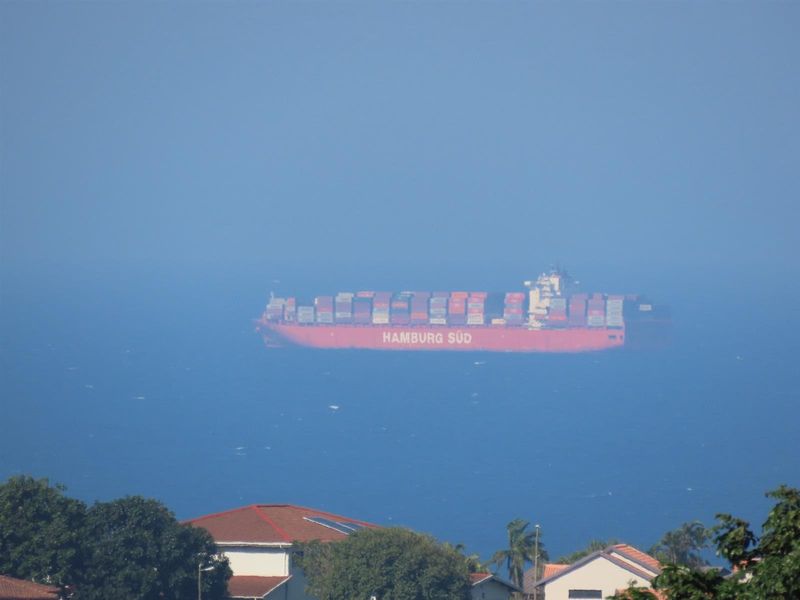 A distant view of a cargo ship on the ocean, captured from an elevated position overlooking residential rooftops.