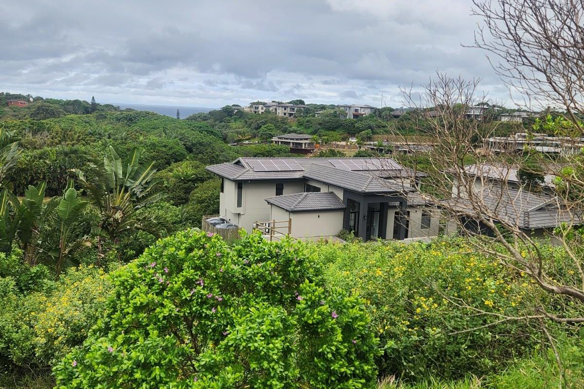 Elevated view of a modern residential property nestled within a lush, green landscape with distant coastal scenery.