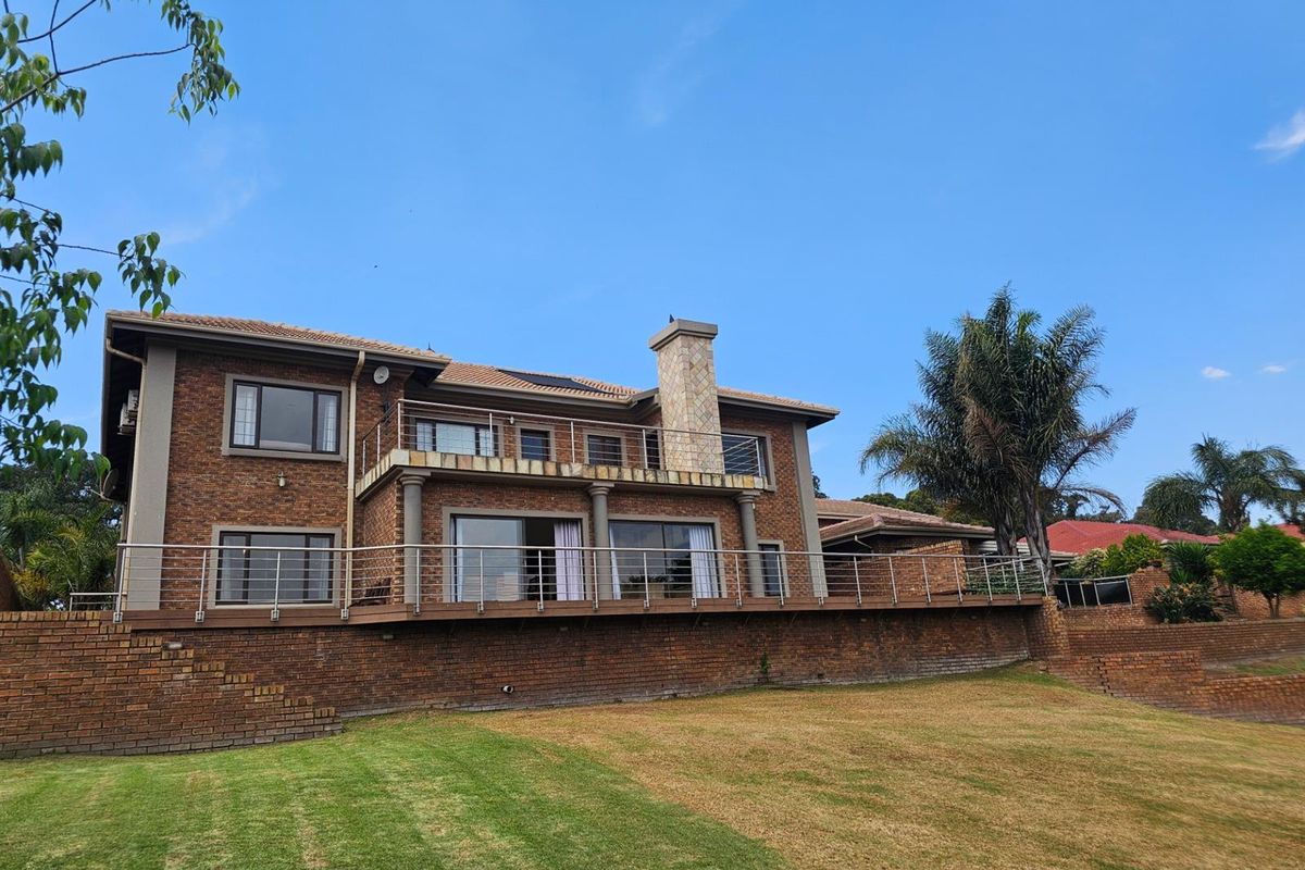 Rear view of a double-story brick house featuring a large elevated wooden deck with stainless steel railings and a stone-clad chimney.