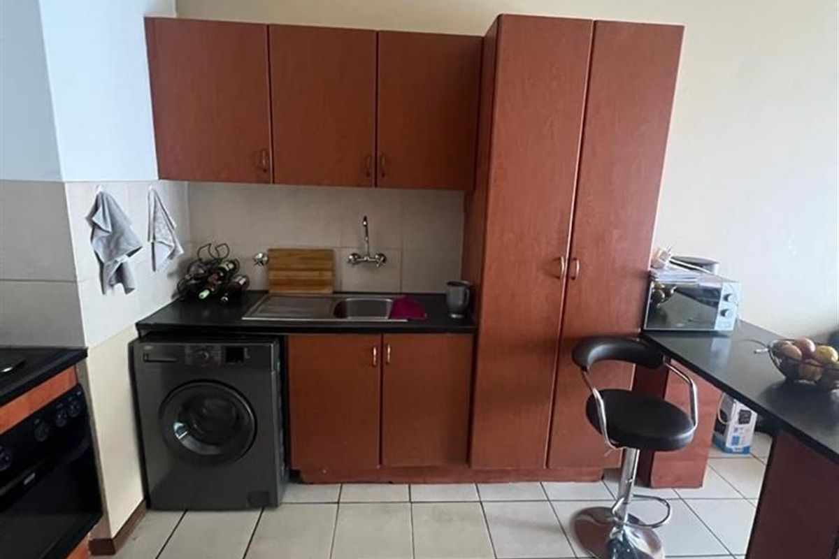 Compact kitchen featuring dark wood-look cabinetry, integrated sink, tiled flooring, and built-in oven, offering a functional layout for an apartment setting.