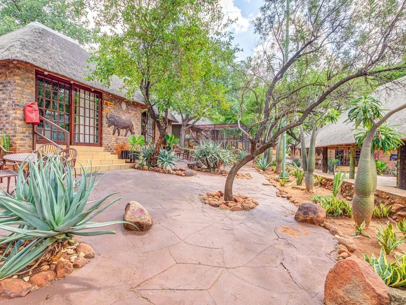 A well-maintained outdoor courtyard area featuring face brick buildings with traditional thatched roofs, paved walkways, and established garden landscaping.