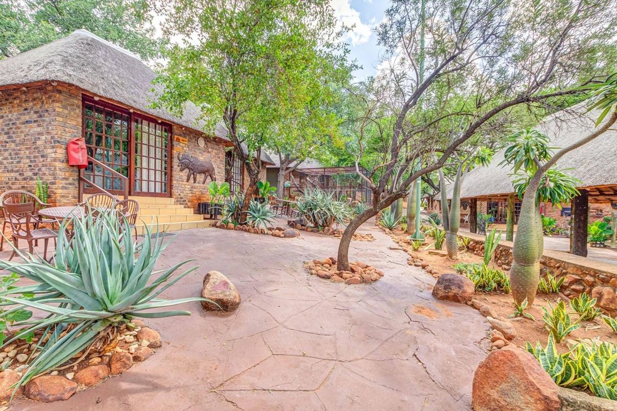 A well-maintained outdoor courtyard area featuring face brick buildings with traditional thatched roofs, paved walkways, and established garden landscaping.