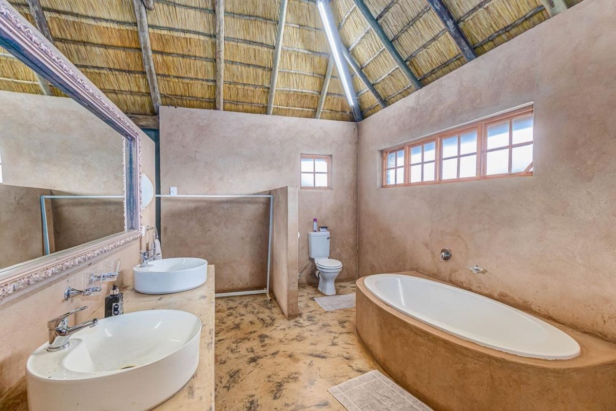 Spacious bathroom featuring a double vanity, built-in bathtub, toilet, and unique exposed thatch roof with rustic concrete wall and floor finishes.