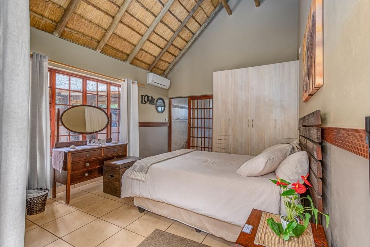 A cozy bedroom featuring a high vaulted thatch ceiling with exposed rafters, built-in cabinetry, tiled floors, and a split-system air conditioner.