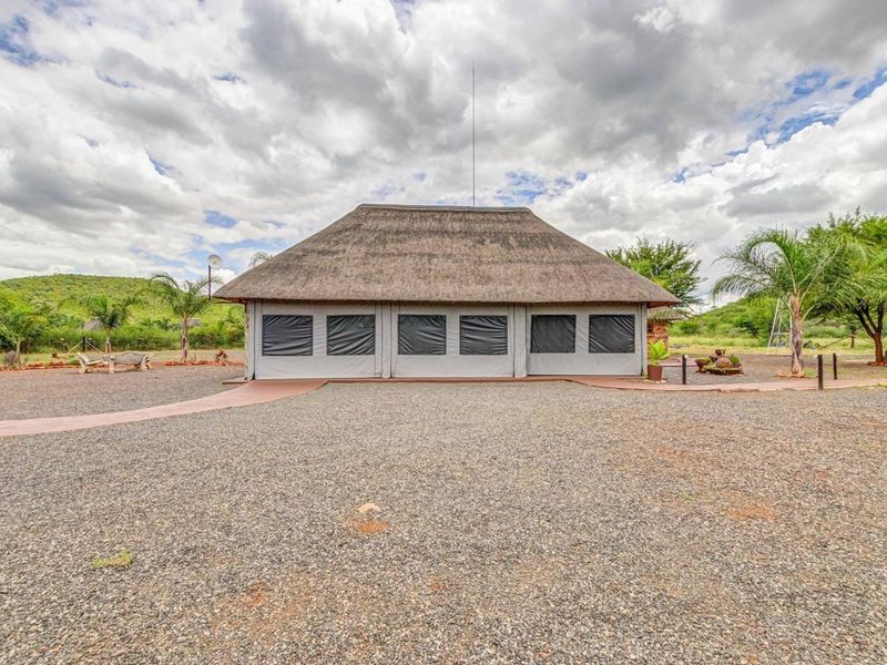 A commercial property featuring a structure with a traditional thatch roof and roll-up canvas walls, set within a spacious gravel-surfaced outdoor area.