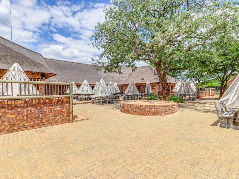 Spacious outdoor courtyard area featuring brick paving, a circular brick planter, and traditional thatched roof architecture, ideal for commercial hospitality use.