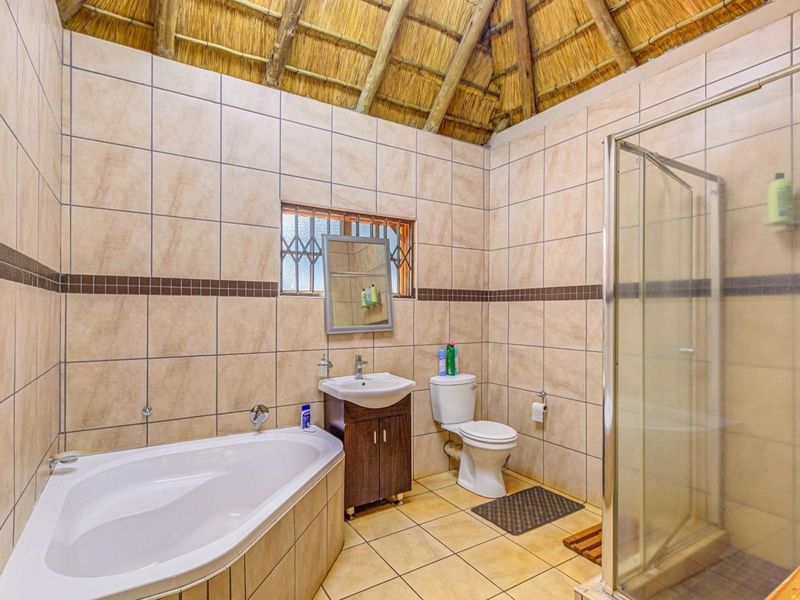 A bathroom featuring a corner bathtub, glass shower enclosure, vanity cabinet, and toilet, finished with tiled walls and a traditional thatched roof ceiling.