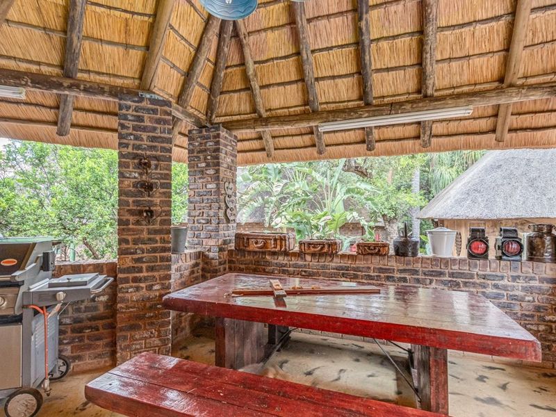 Covered outdoor entertainment area featuring a traditional thatched roof, exposed timber rafters, and rustic face brick construction, ideal for alfresco dining.