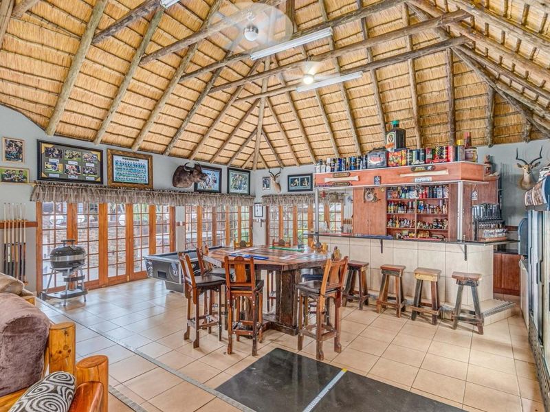 Spacious entertainment area featuring a built-in bar, high thatched ceiling with exposed timber rafters, tiled flooring, and large wooden folding doors leading outdoors.