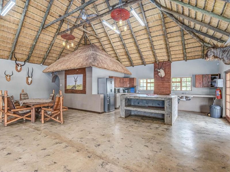 Spacious open-plan commercial area featuring a high thatched roof with exposed rafters, a central concrete island, and integrated kitchen facilities.