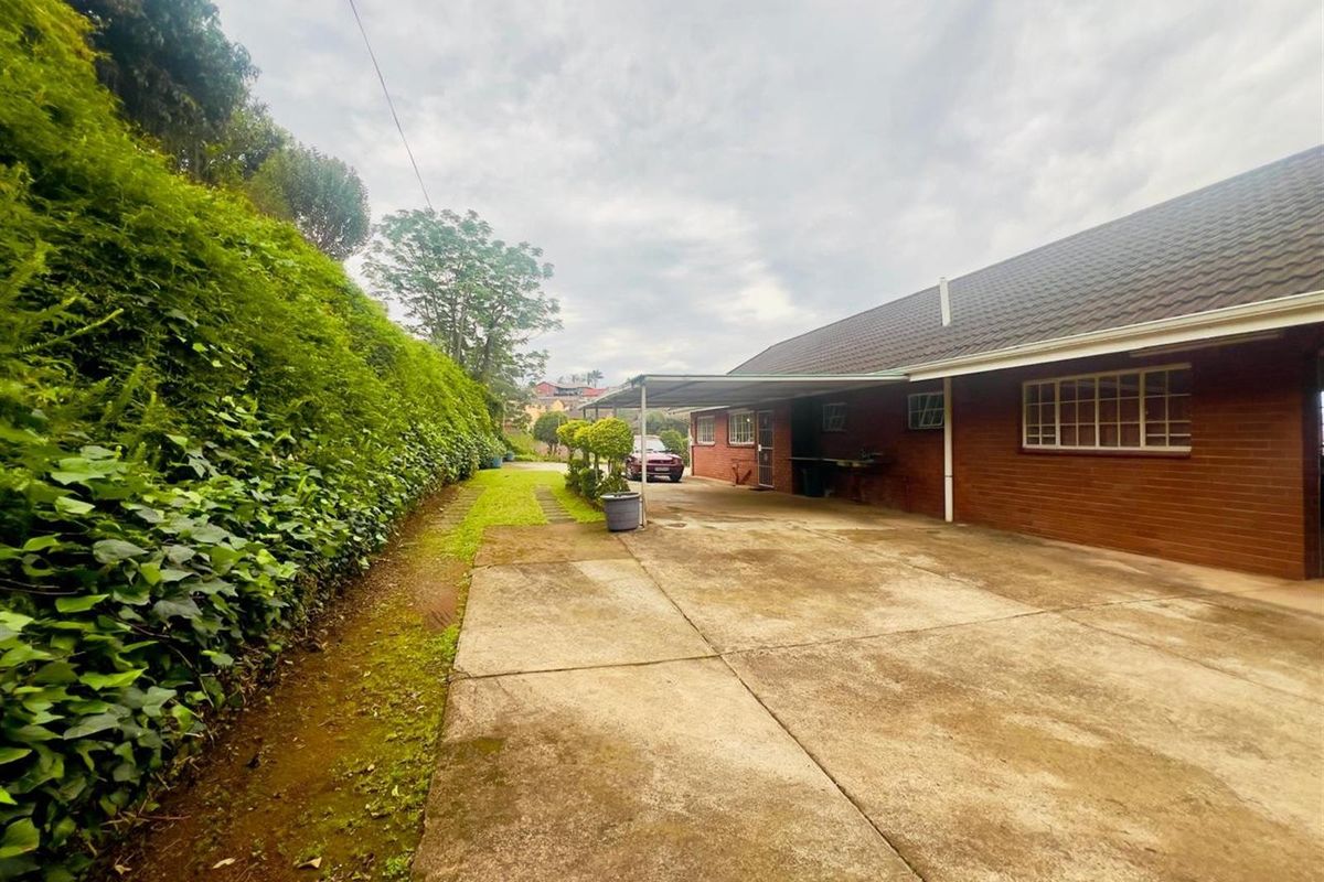 Exterior view of the side of the house featuring a concrete driveway, a covered carport area, and a landscaped embankment.