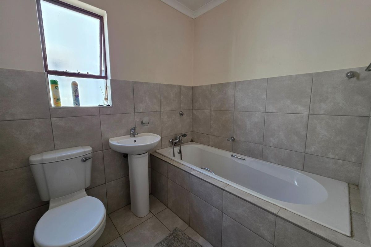 A functional bathroom featuring a pedestal sink, a standard bathtub with tiled surround, and a toilet, finished with neutral wall tiles.