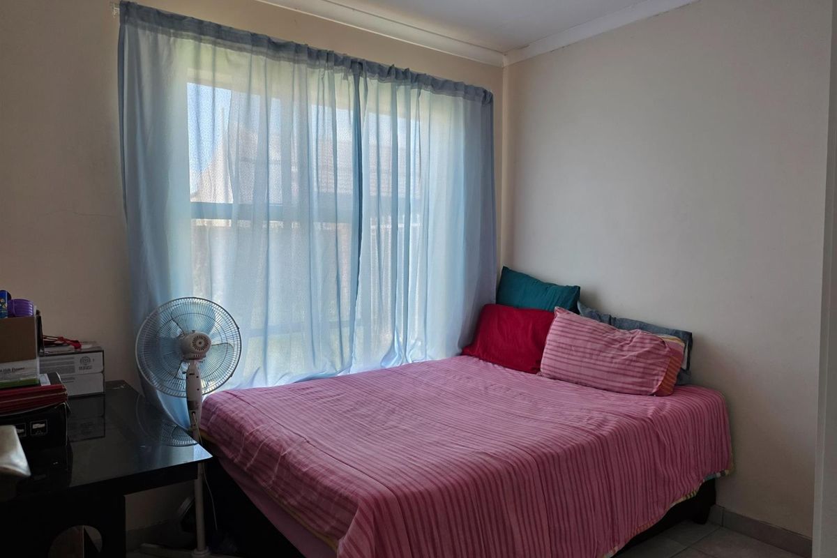 A functional bedroom featuring tiled flooring and a window with sheer curtains, providing natural light.