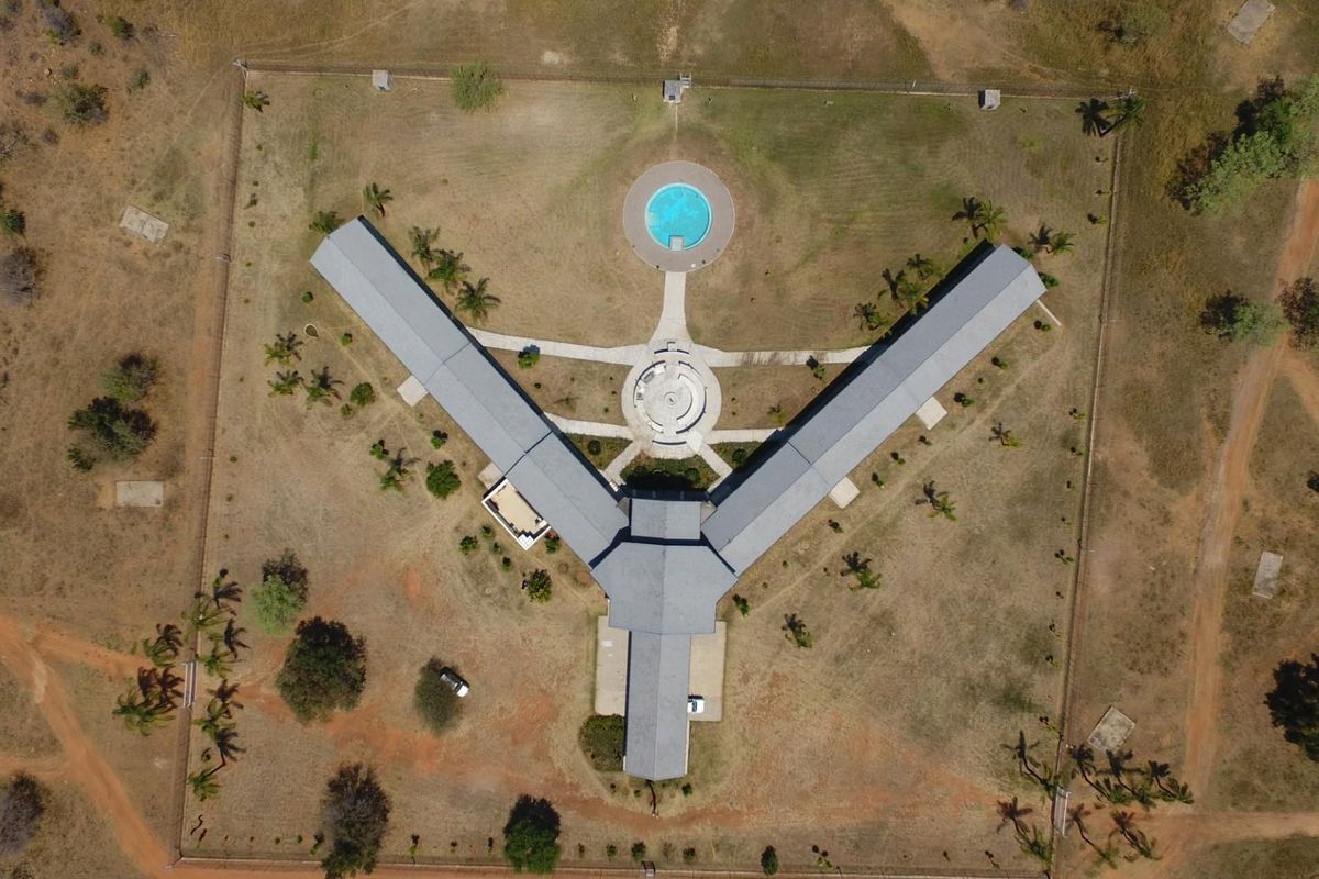 Aerial view of a large farm property featuring a Y-shaped building layout, a circular swimming pool, and extensive surrounding grounds.