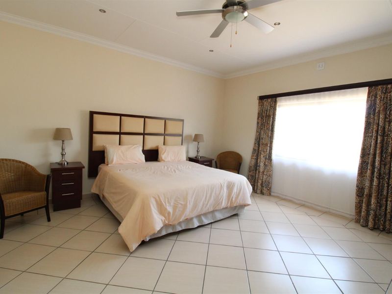 Spacious bedroom featuring tiled flooring, a ceiling fan, and large windows with curtain tracks.