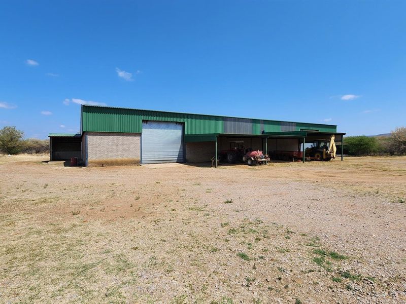 Large agricultural shed featuring a roller shutter door and an attached open-sided machinery storage bay on a rural farm property.