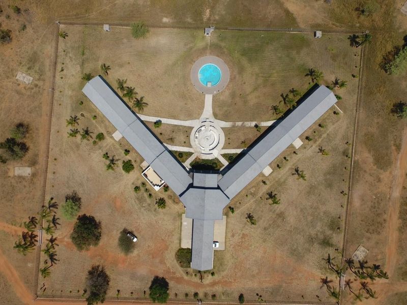 Aerial view of a large farm property featuring a Y-shaped building layout, a circular swimming pool, and extensive surrounding grounds.