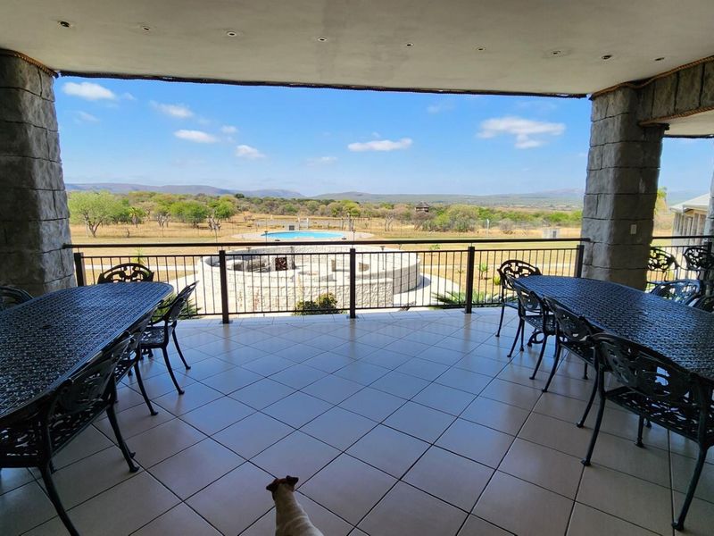 Spacious covered patio featuring stone-clad pillars, tiled flooring, and expansive views overlooking the farm landscape and swimming pool area.