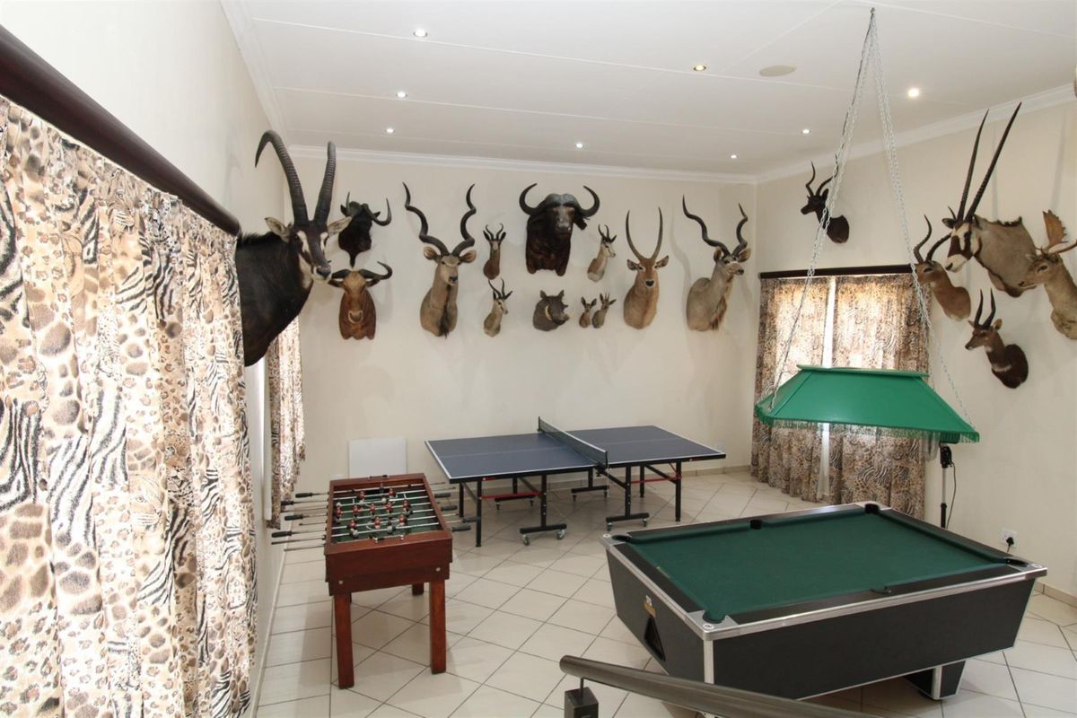 A spacious entertainment room featuring tiled flooring, recessed ceiling lighting, and ample wall space, currently utilized as a games room.