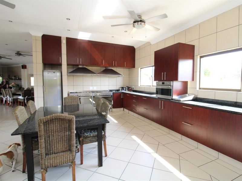 Spacious open-plan kitchen featuring dark wood cabinetry, granite countertops, dual stainless steel stoves, and integrated oven, seamlessly flowing into the dining area.