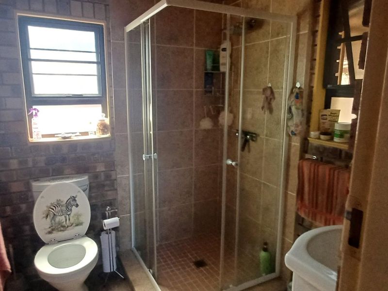 A functional bathroom featuring a shower enclosure, toilet, and pedestal basin, finished with tiled surfaces and rustic exposed brick walls.