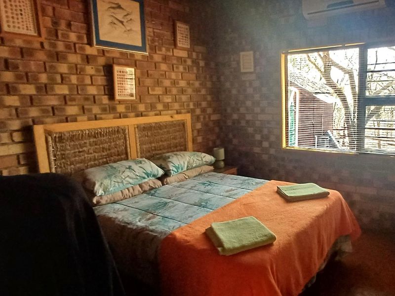A cozy bedroom featuring rustic exposed brick walls, an integrated air conditioning unit, and a window with security bars.