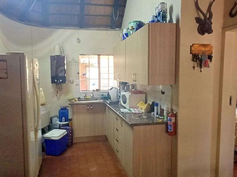 A compact kitchen featuring built-in cabinetry, laminate countertops, and a stainless steel sink, set under a traditional thatched roof structure.