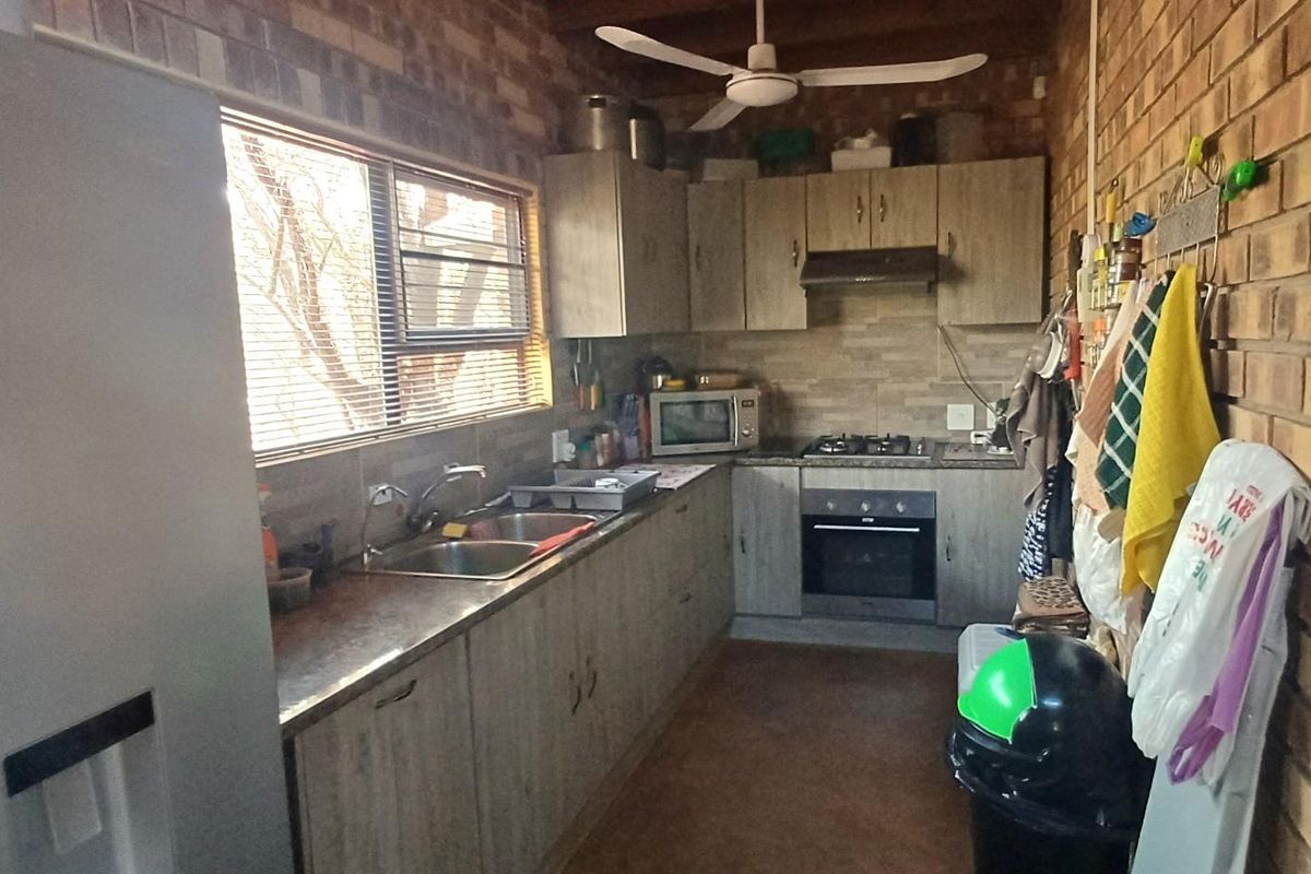 A functional kitchen featuring exposed brick walls, wood-look cabinetry, gas hob, built-in oven, and a double sink with a window view.