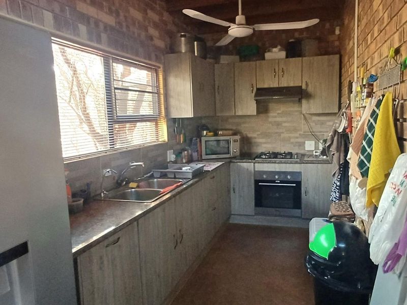 A functional kitchen featuring exposed brick walls, wood-look cabinetry, gas hob, built-in oven, and a double sink with a window view.