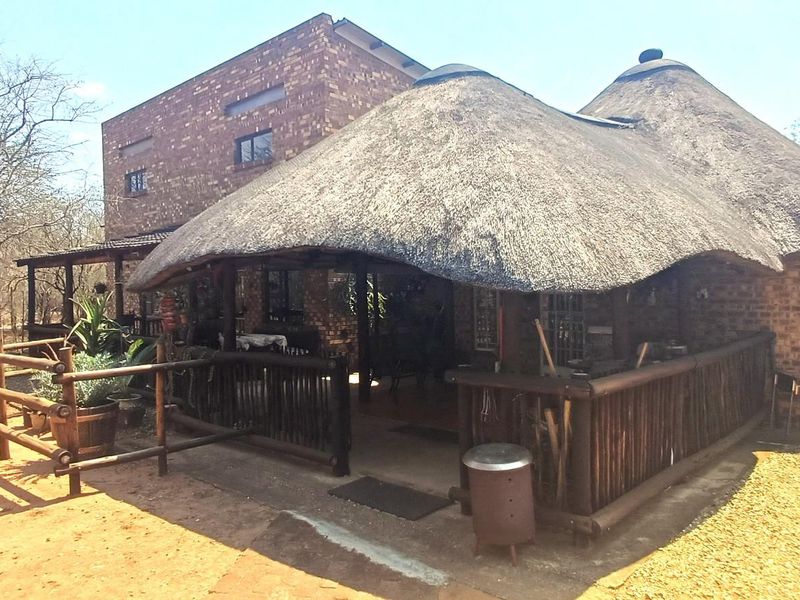 Rear view of a rustic brick house featuring a traditional thatch roof and a covered timber deck patio area.