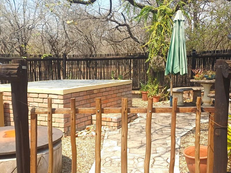 Outdoor pool area featuring a brick-surrounded pool, paved pathways, and rustic timber fencing set within a natural garden environment.